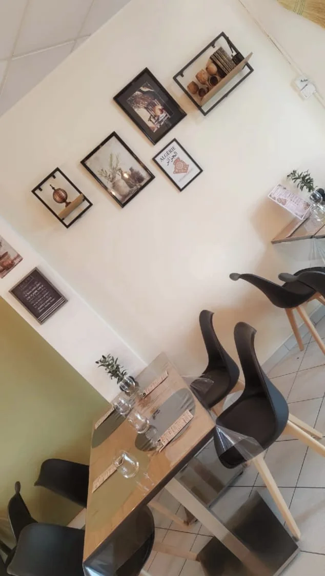 Coin salle : tables en bois clair, chaises noires et cadres accrochés au mur