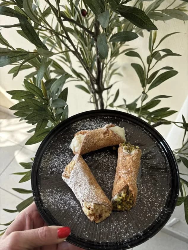 Deux cannoli garnis de ricotta et de pistaches, saupoudrés de sucre glace