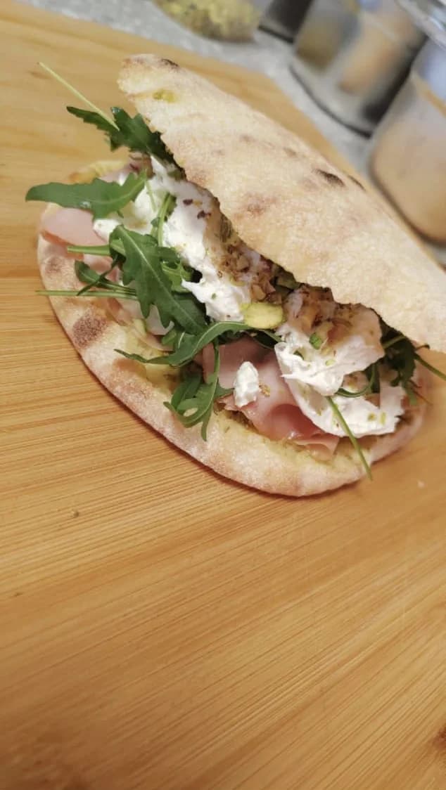 Puccia ouverte garnie de jambon cru, burrata et roquette, posée sur une planche en bois